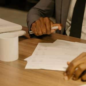 Free Close-up of a businessman holding and reviewing documents on a wooden desk. Stock Photo